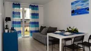 Een moderne woonkamer met een bank, een eettafel met stoelen, een blauw bureau en een schilderij aan de muur.