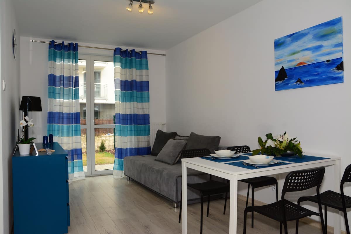 Un salon moderne avec un canapé, une table à manger et des chaises, un bureau bleu et un tableau accroché au mur.