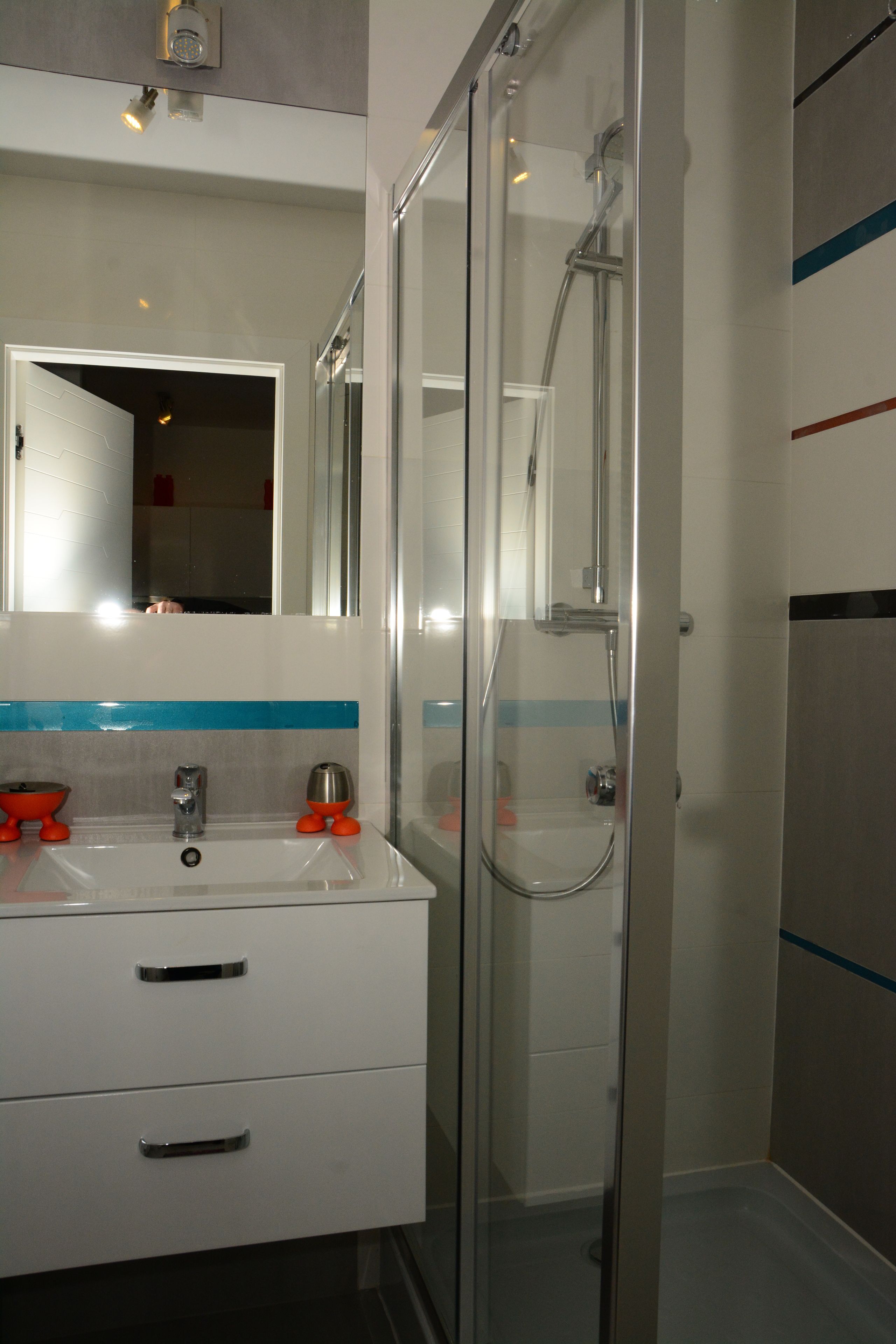 Une salle de bain avec une douche à parois de verre, un lavabo blanc doté de deux tiroirs et un miroir au-dessus du lavabo.