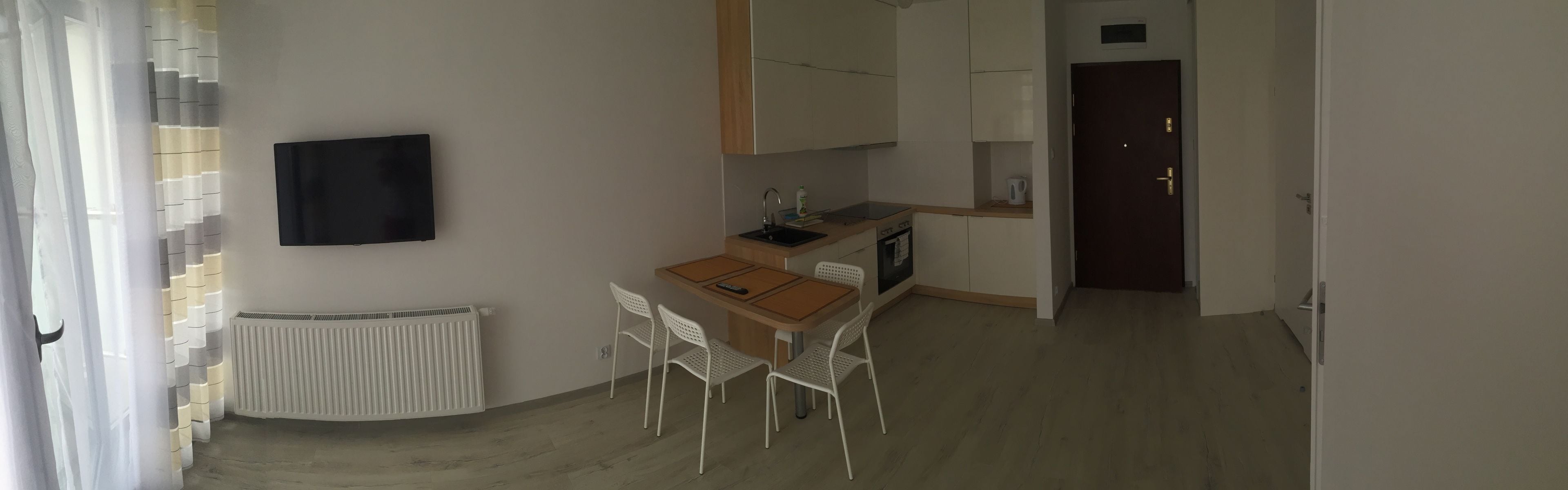 Un espacio diáfano y acogedor que combina sala y comedor, con kitchenette, un radiador y un televisor montado en la pared.