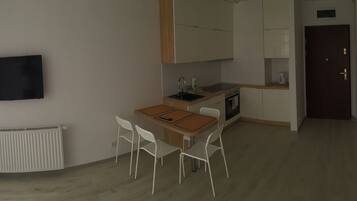 Un espacio diáfano y acogedor que combina sala y comedor, con kitchenette, un radiador y un televisor montado en la pared.
