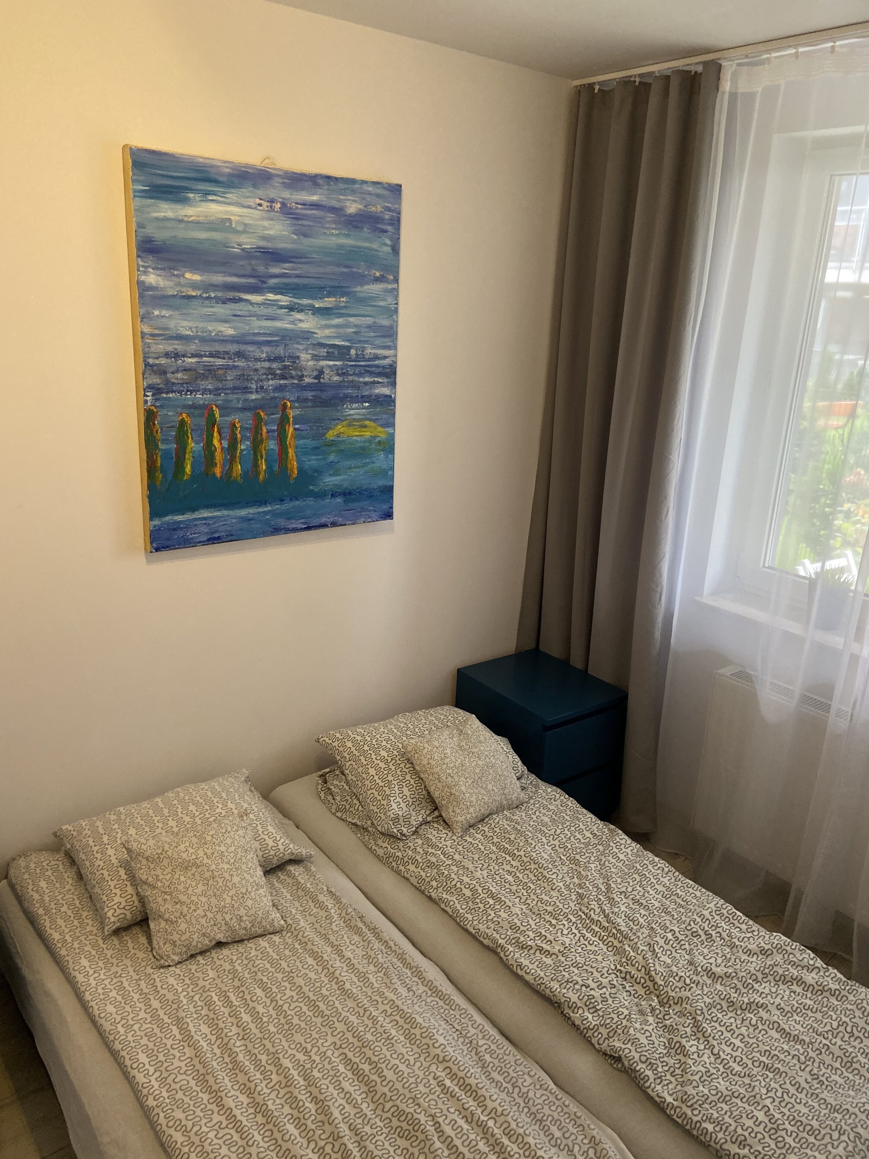 Una stanza con due letti singoli, un quadro appeso al muro, un tavolino e una finestra con tende.