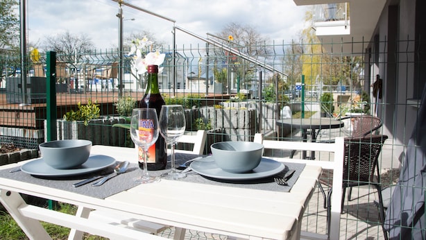 Een terras met een eettafel gedekt voor twee personen, een fles wijn en een glas.