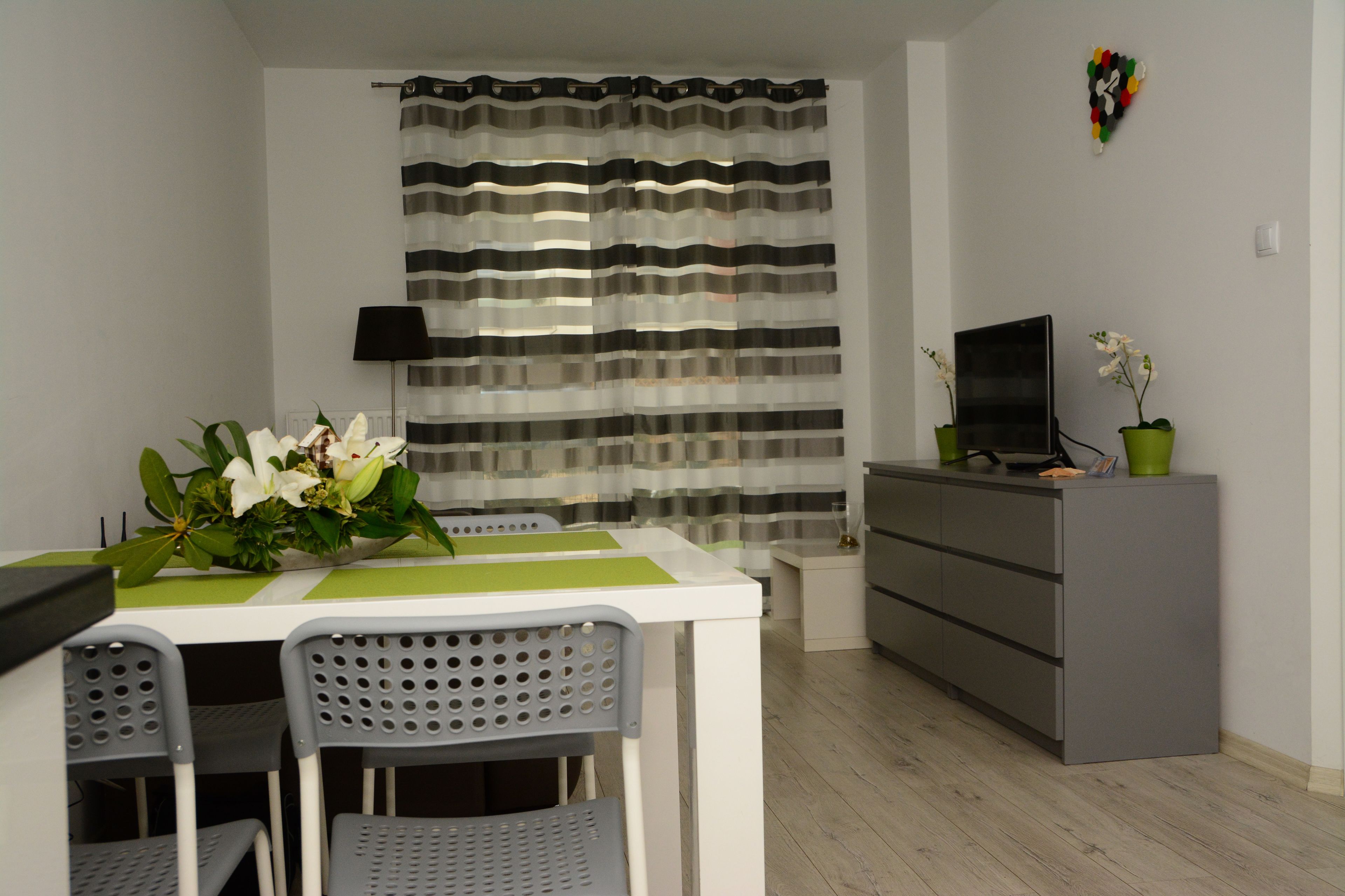 A modern living room with a dining table, chairs, a TV, and a grey cabinet.