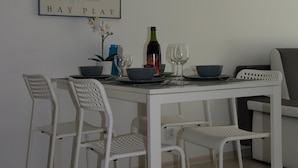 Een eethoek met een witte tafel, vier witte stoelen, een lijst met een afbeelding aan de muur en een fles wijn.