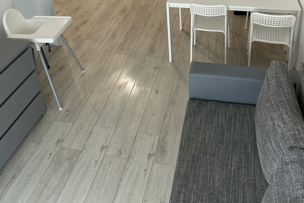 Un espace de vie compact comprenant un coin cuisine, un coin repas avec une table et des chaises, un canapé et une petite chaise blanche.