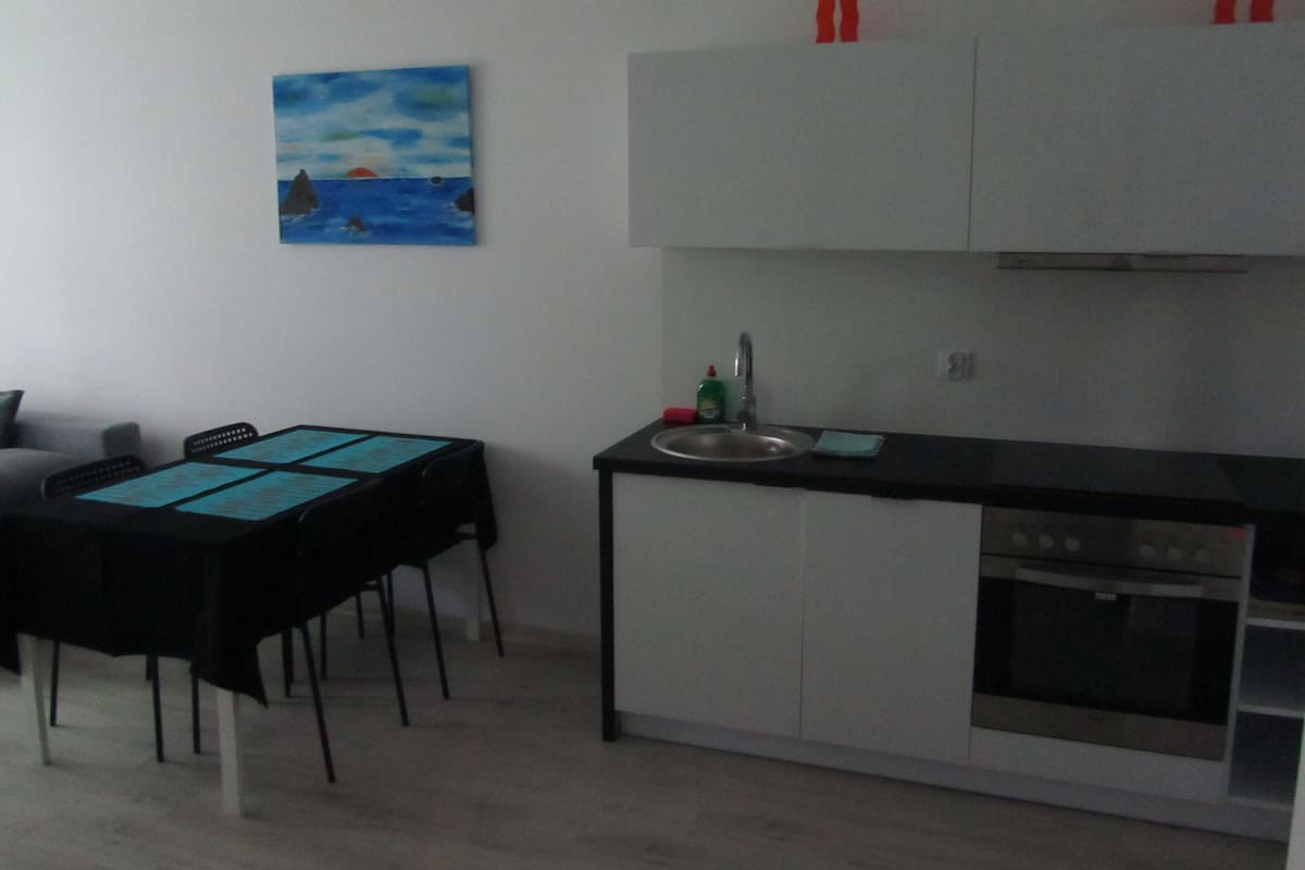 Une cuisine compacte avec un coin repas, comprenant une table noire, des placards blancs et un tableau accroché au mur.