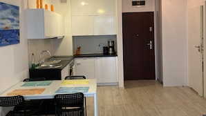 Een kleine keuken met witte kastjes, een eettafel met stoelen en een donker houten deur.