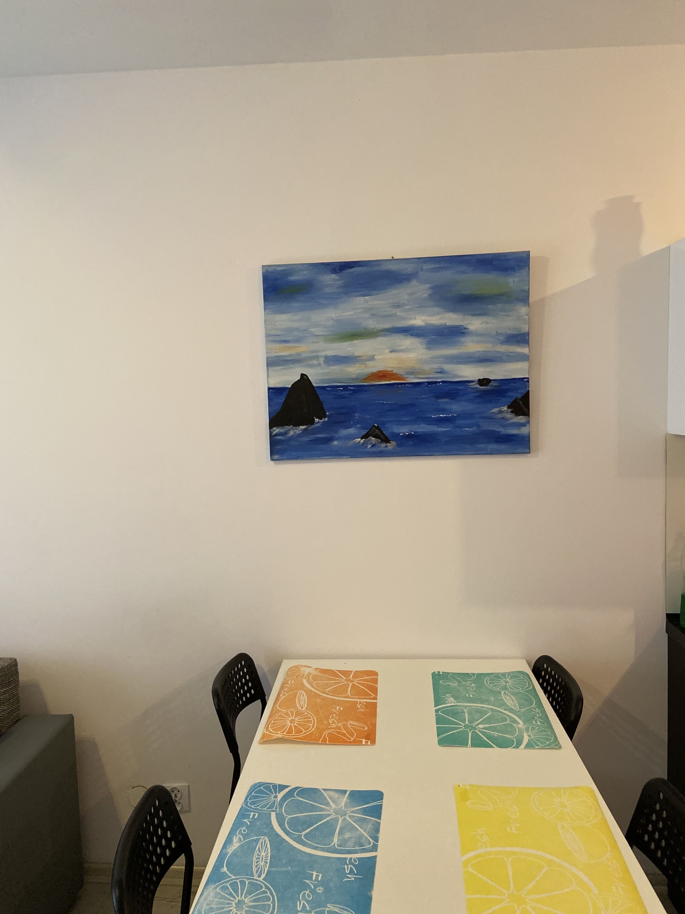 Ein Essbereich mit Tisch für vier Personen, Stühlen und einem an der Wand hängenden Meeresblick-Gemälde.