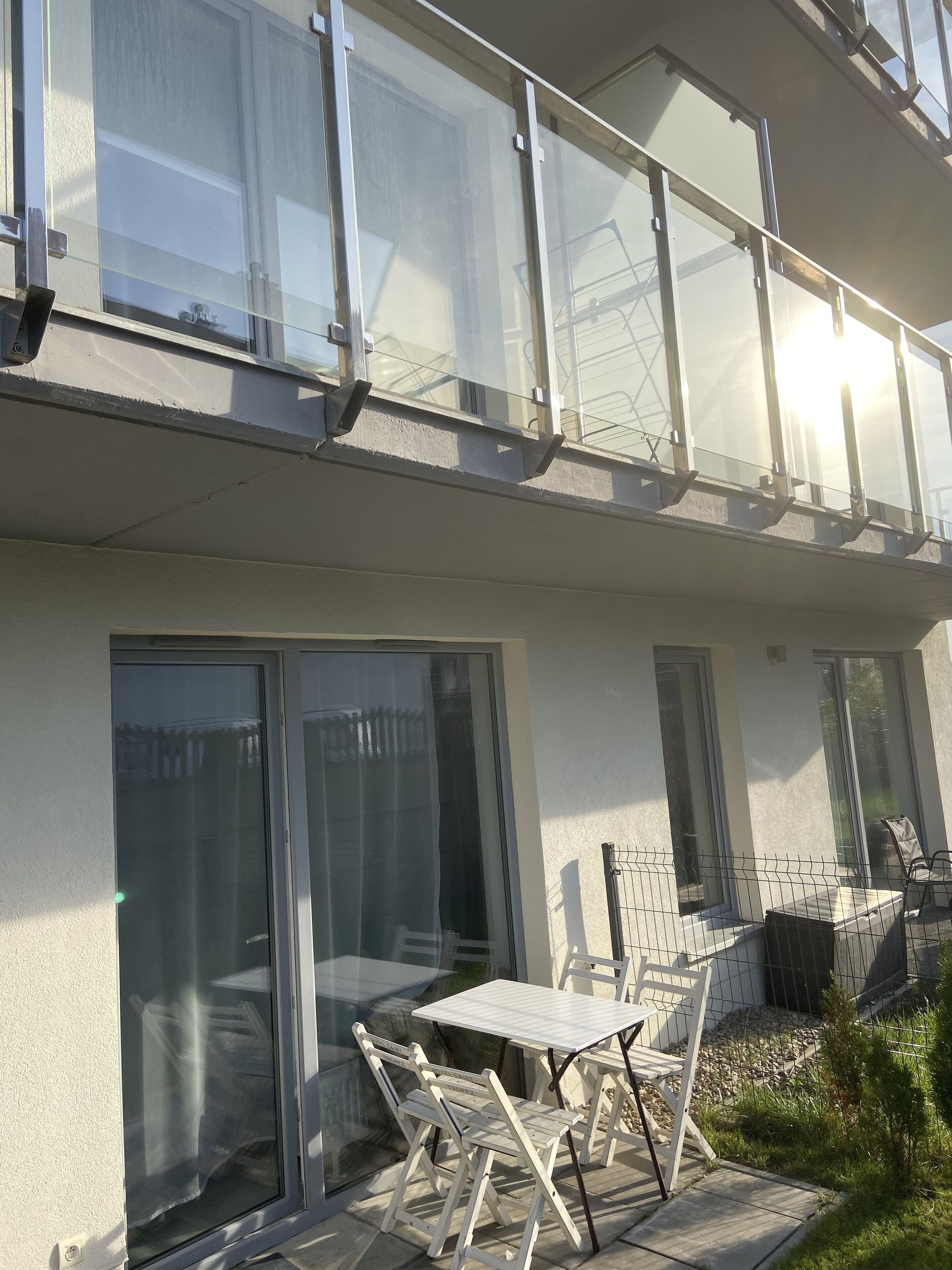 Un edificio moderno con balcón, ventanas amplias y mobiliario exterior.