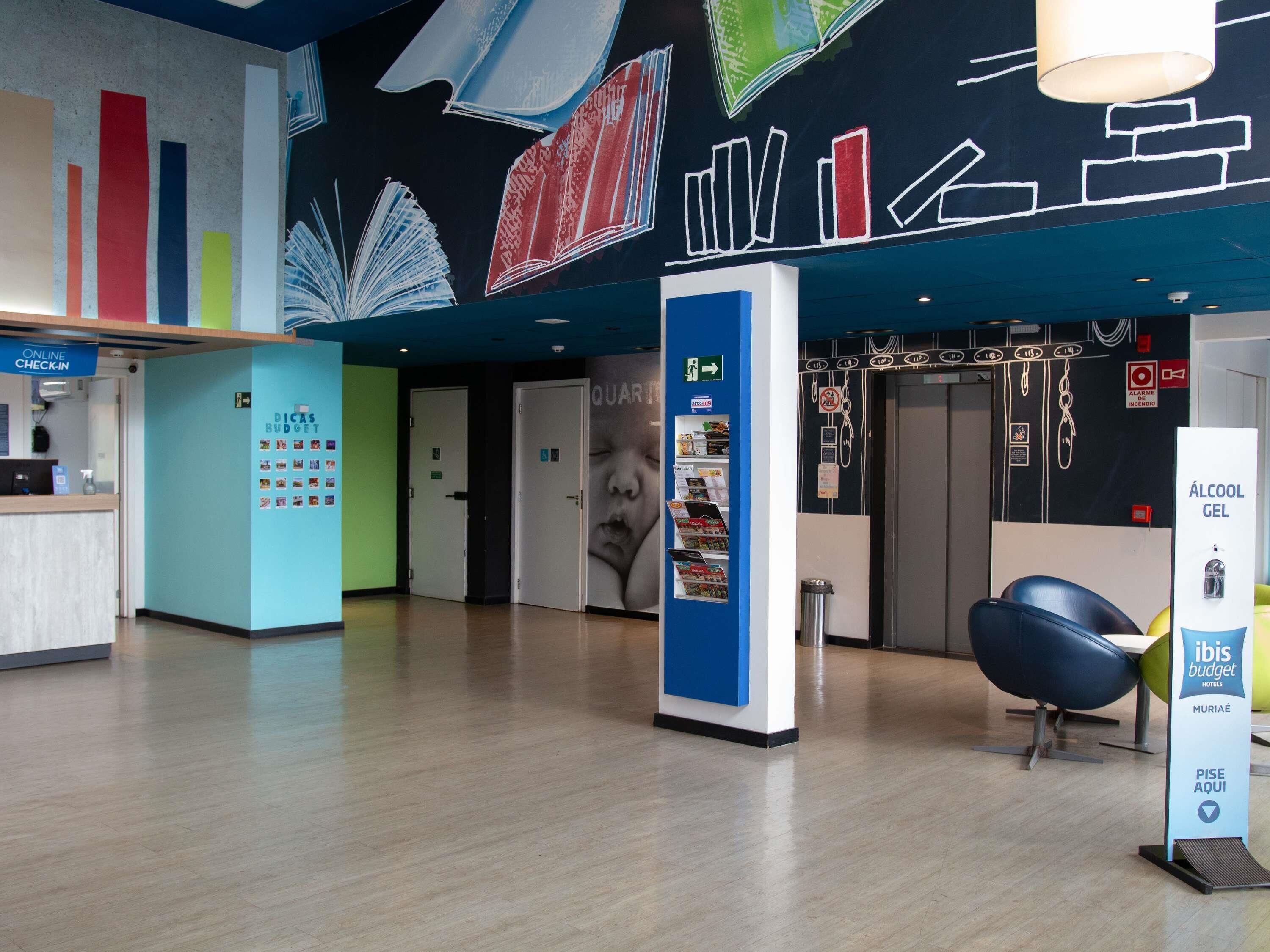 A hotel lobby with a reception desk, a blue information kiosk, and a wall with a cityscape mural.
