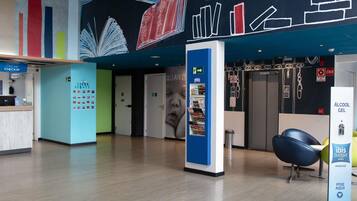 A hotel lobby with a reception desk, a blue information kiosk, and a wall with a cityscape mural.