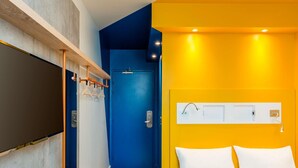 A hotel room with a bed, a door, a wall-mounted light, and a wooden shelf. - ibis budget Muriae (Muriae)