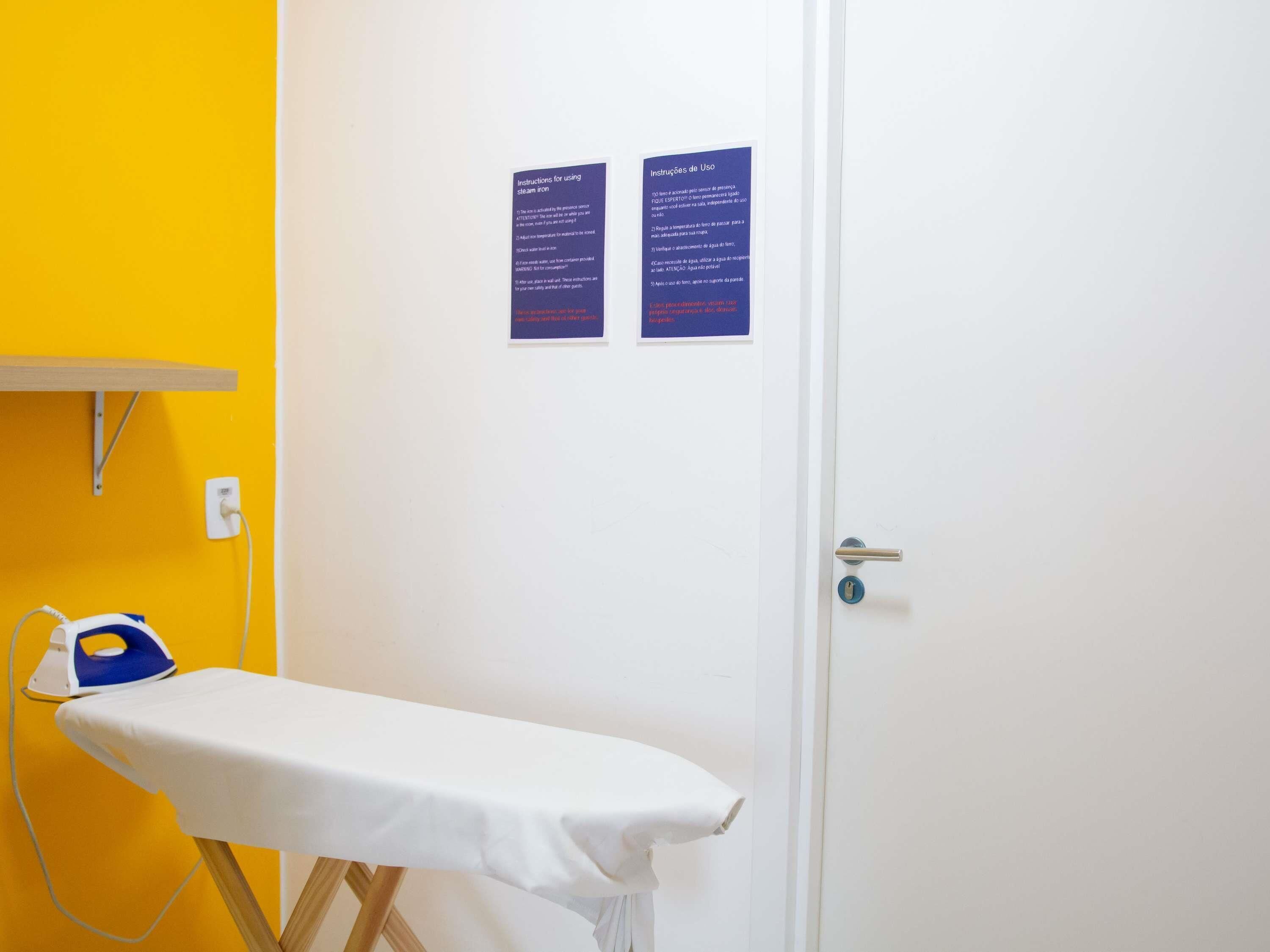 A room with a white ironing board, a yellow wall, and a white door. There are two instruction signs on the door.