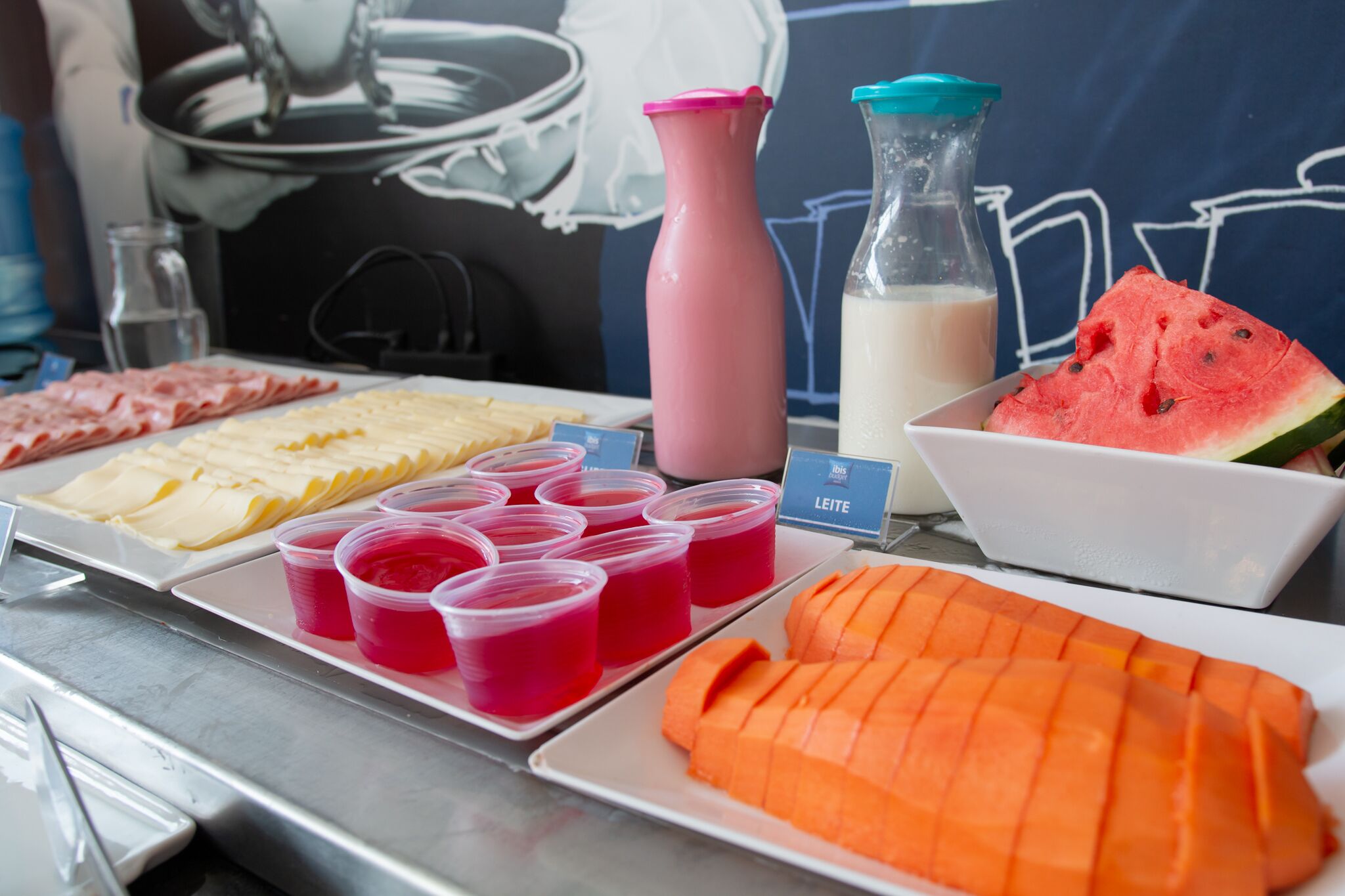 Ein Büfett mit verschiedenen Speisen, darunter Wassermelone, Mango und Käse, sowie mehreren Getränken.