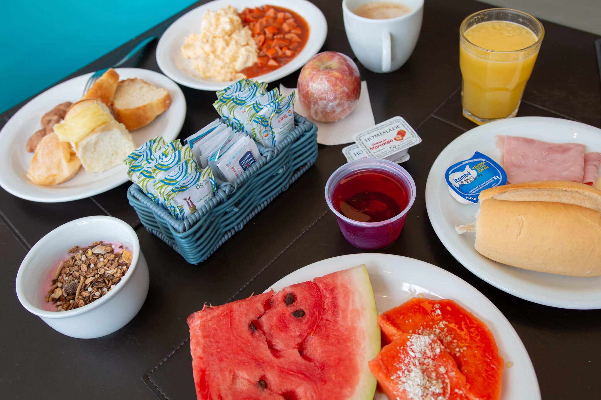 A breakfast table with various food items including bread, eggs, a slice of watermelon, and a glass of orange juice.