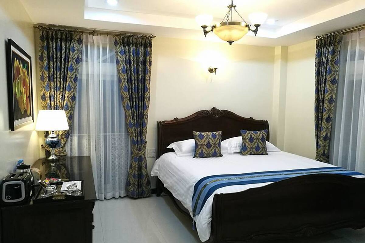 A hotel room with a large bed, a bedside table with a lamp, and curtains.