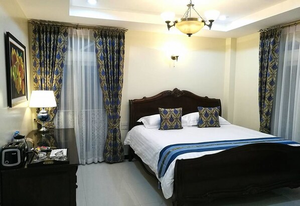 A hotel room with a large bed, a bedside table with a lamp, and curtains.