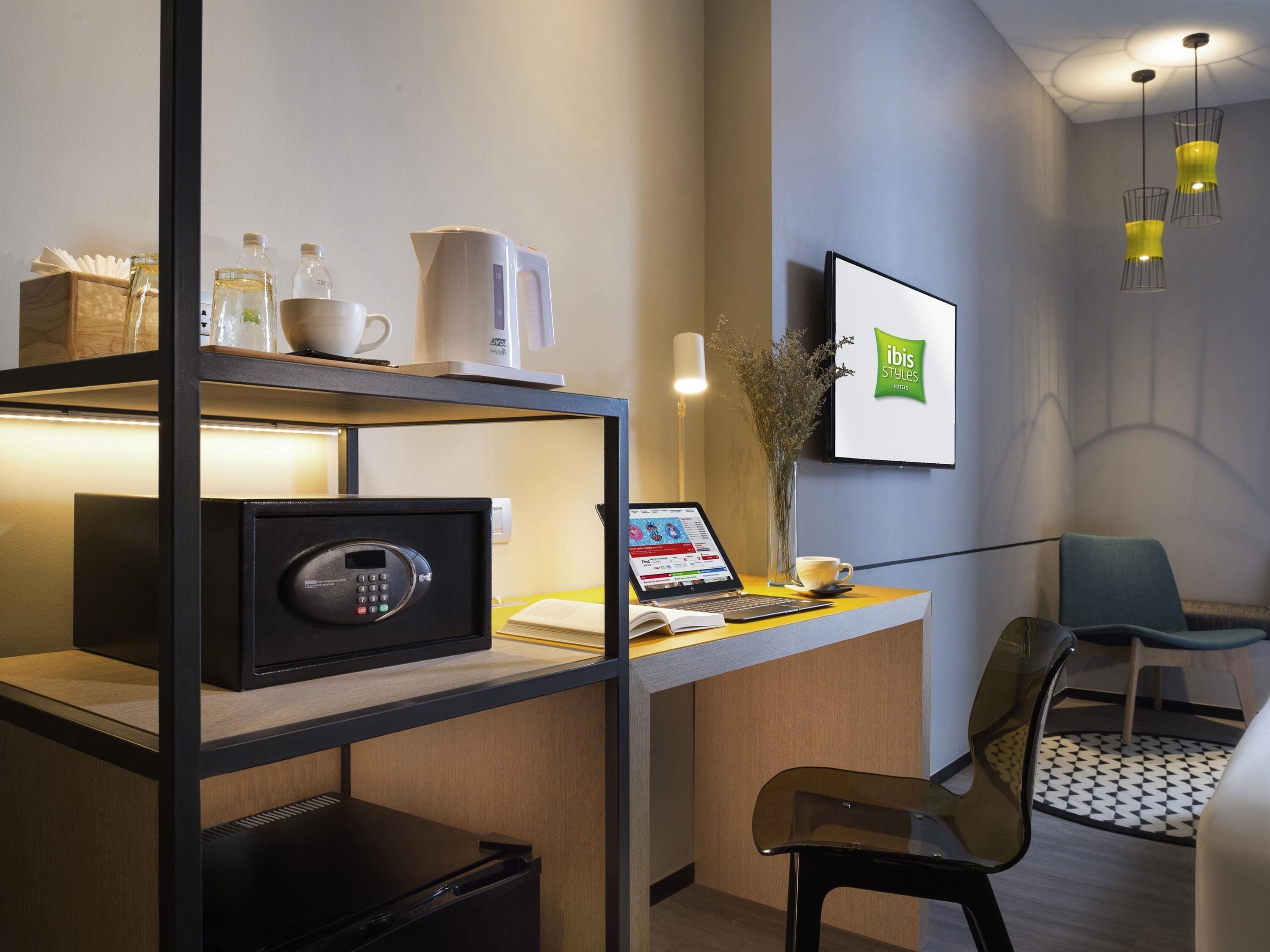 Une chambre d’hôtel moderne équipée d’un bureau, d’un ordinateur portable, d’une tasse à café, d’un vase avec des fleurs, d’un tableau encadré et d’une chaise.