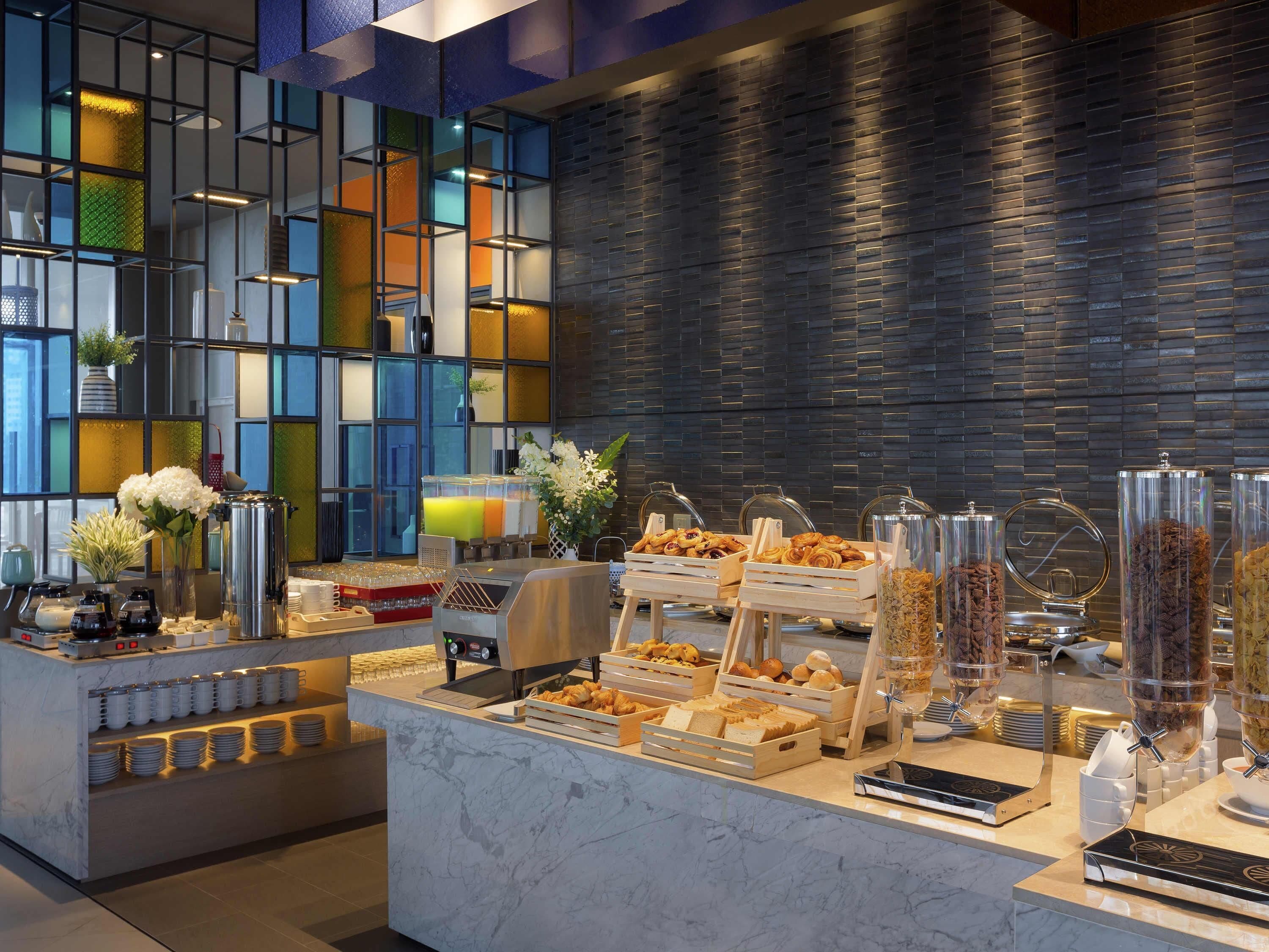 Un área de bufé con diversos alimentos, una estación de café y una pared decorativa con un diseño geométrico.