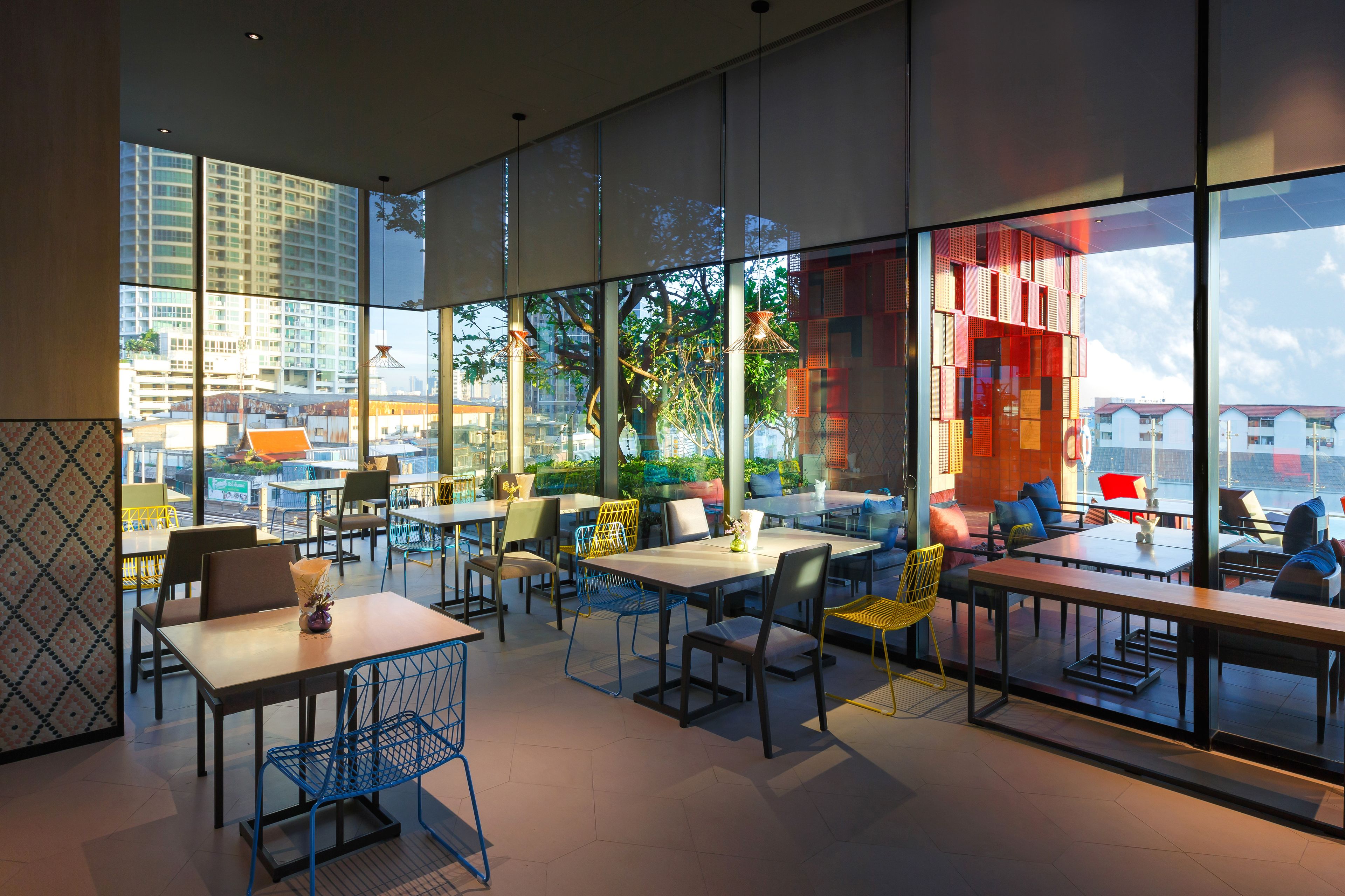 A modern indoor dining area with large windows, multiple tables and chairs, and a view of the cityscape.