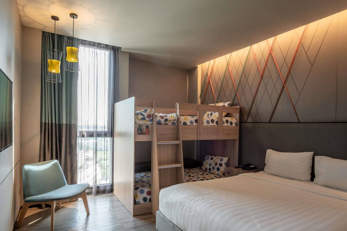 A bedroom with a bunk bed, a single bed, a chair, a desk, and a window with curtains.