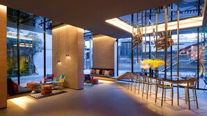 A modern interior with a seating area, a bar, and large windows offering a view of the city. - ibis Styles Bangkok Sukhumvit Phra Khanong (Bangkok)
