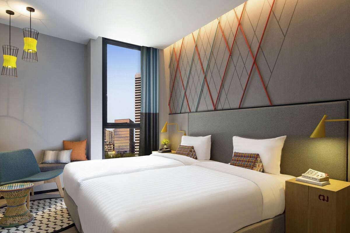 A modern hotel room with a large bed, a view of the city, and a unique geometric wall design.
