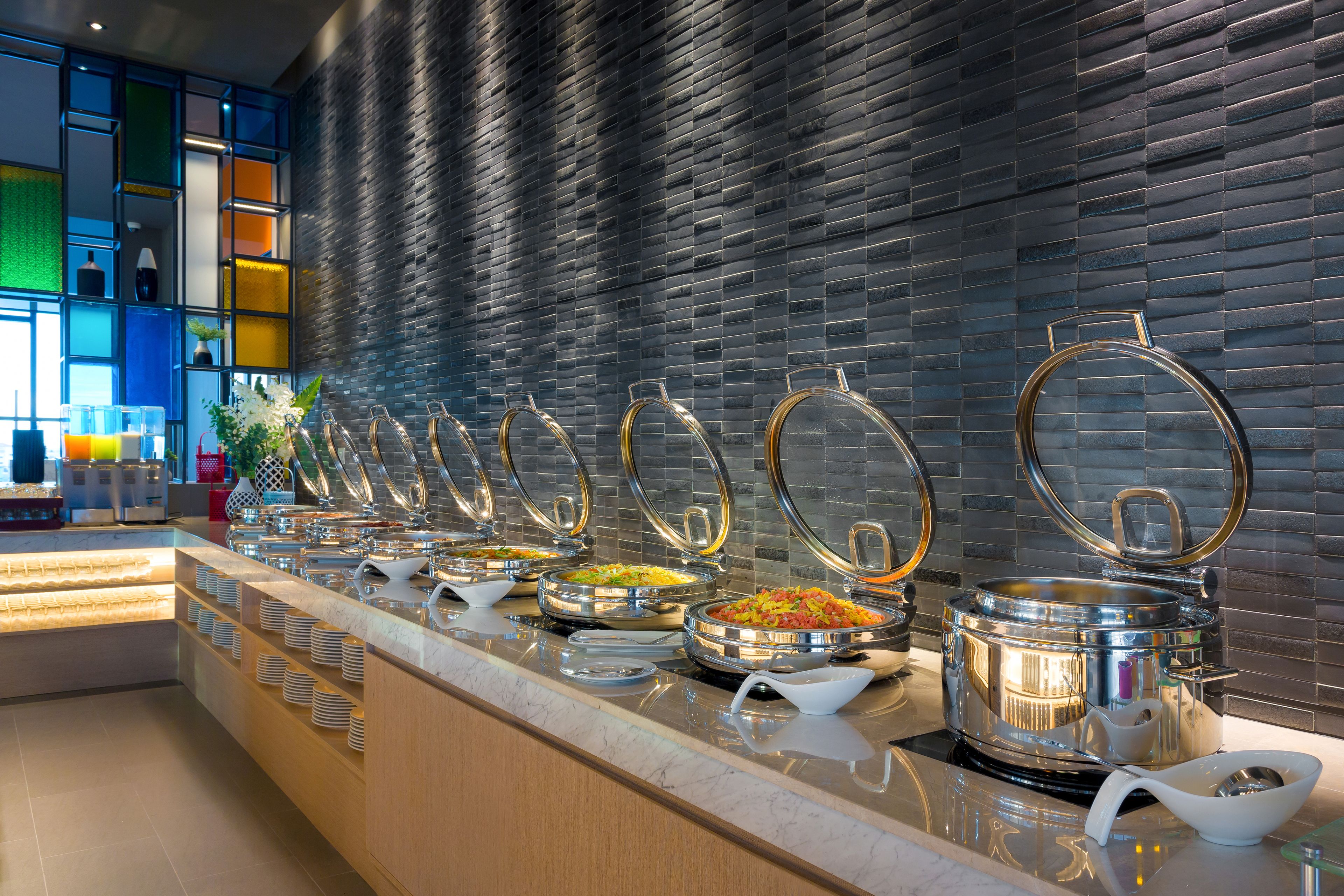 A buffet with various food stations, a marble countertop, and a modern brick wall in the background.