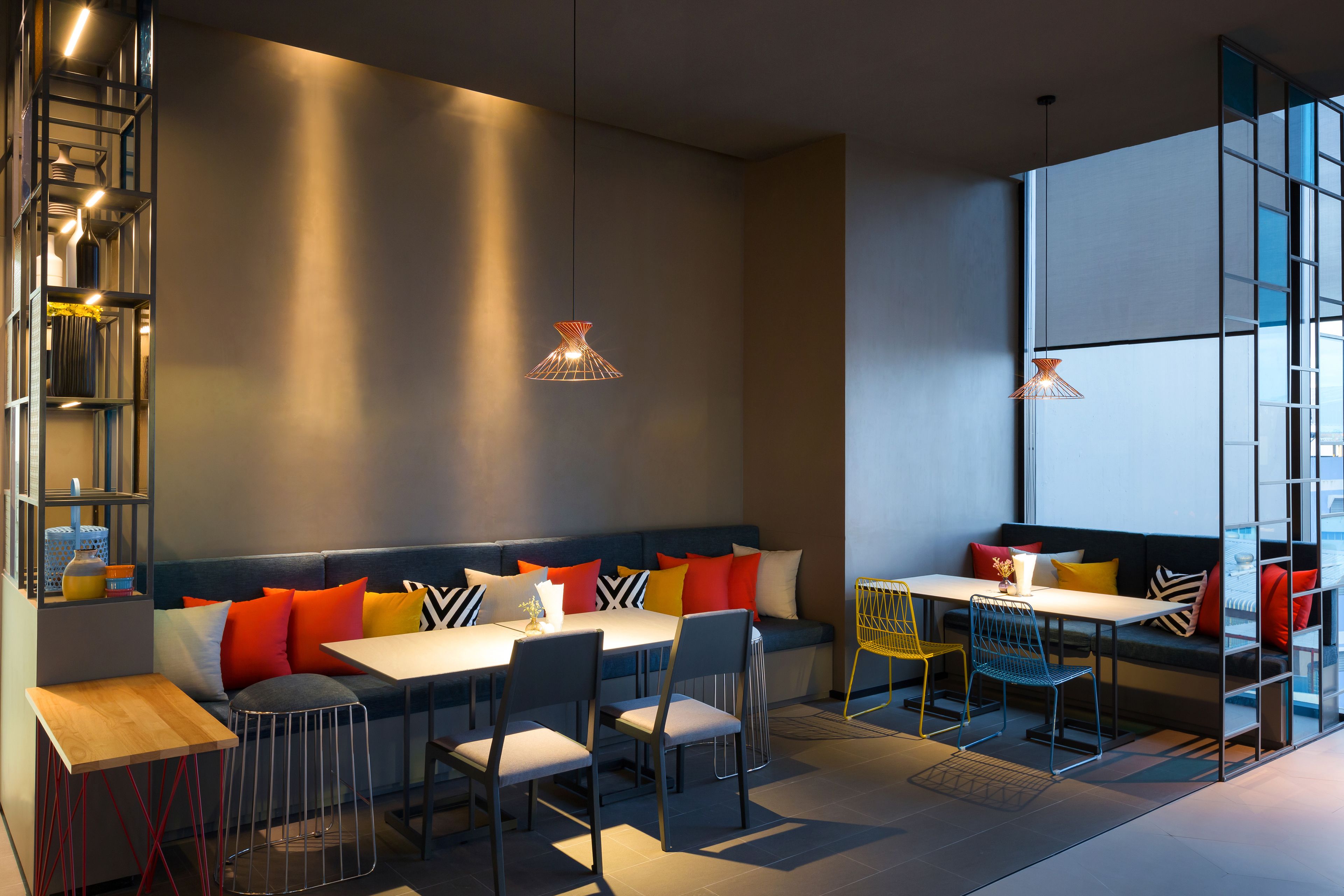 Een moderne eetruimte met een lange tafel, stoelen en een bank met kleurrijke kussens.