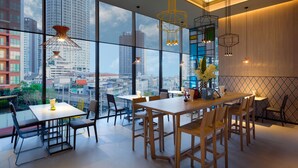 A modern dining area with a city view, featuring a large table and chairs, pendant lighting, and a view of tall buildings through large windows. - ibis Styles Bangkok Sukhumvit Phra Khanong (Bangkok)