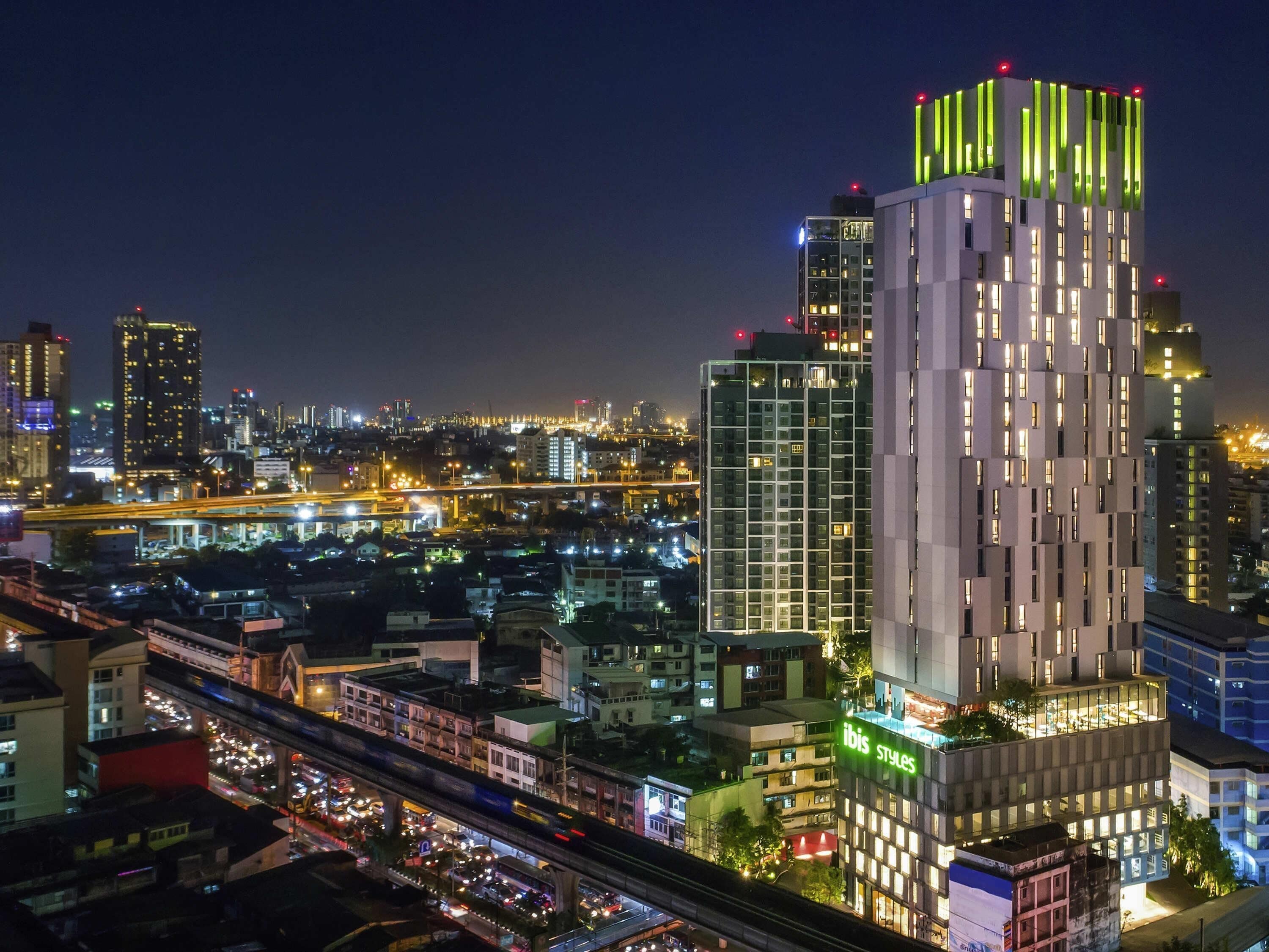 Un immeuble moderne de grande hauteur, doté d’une façade au design original, qui se dresse au milieu d’un paysage urbain animé la nuit.