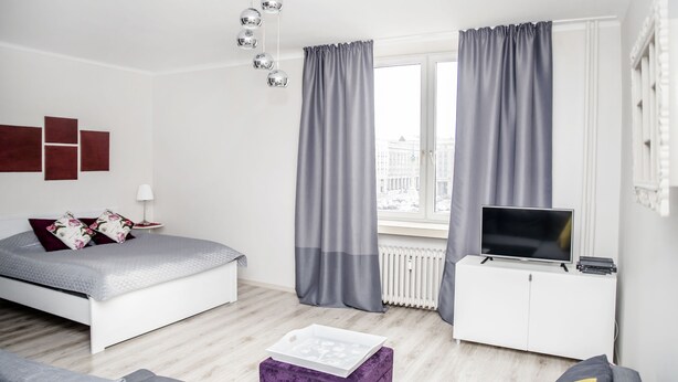 A modern bedroom with a bed, a TV on a white cabinet, and a window with curtains. - AP-Apartments Marszałkowska No. 53 (Warsaw)