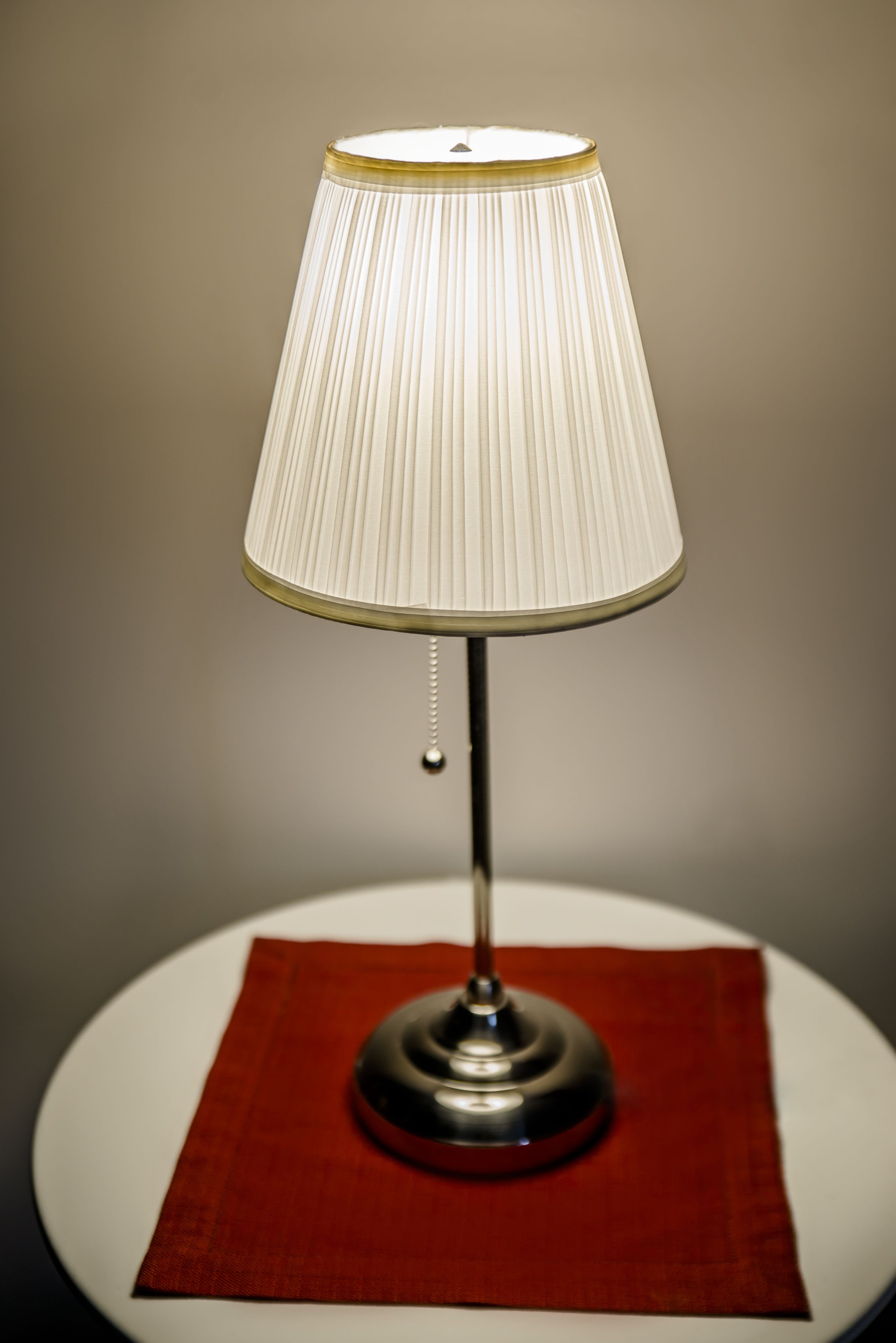 A table lamp with a pleated shade on a white table with a red placemat.