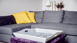 A grey sectional sofa with two yellow pillows, a white tray with a laptop, and a purple ottoman. - AP-Apartments Marszałkowska No. 53 (Warsaw)
