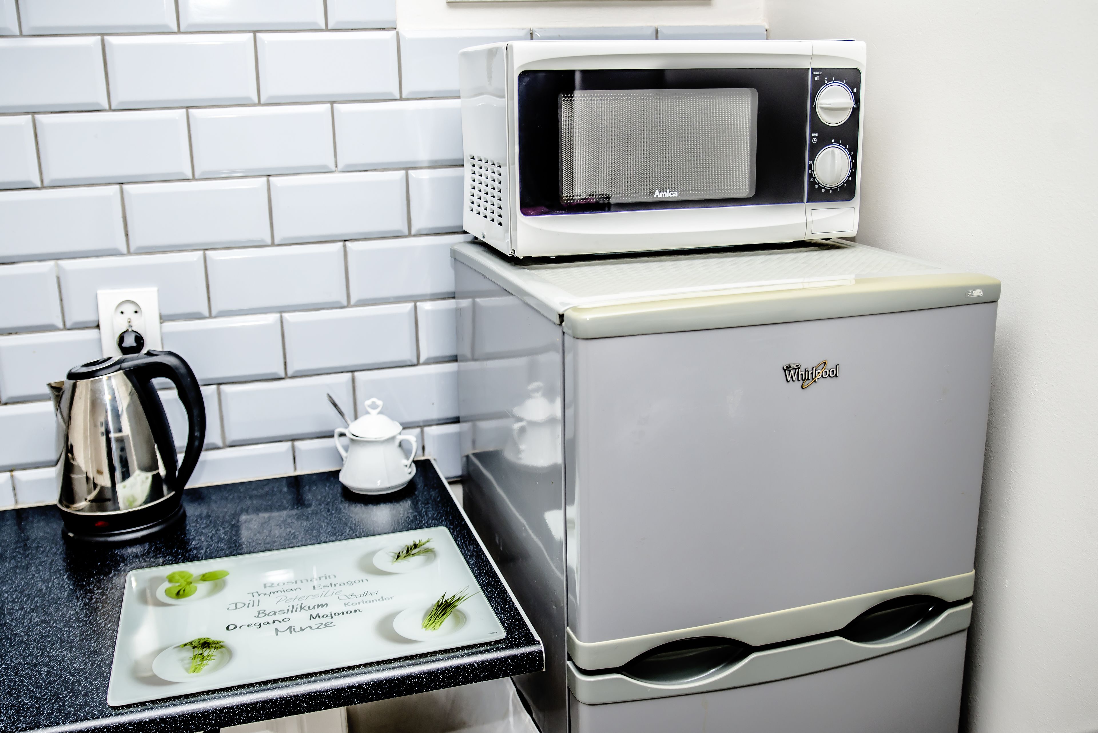 A kitchen with a white refrigerator, a microwave, a kettle, and a small white pitcher on the counter.