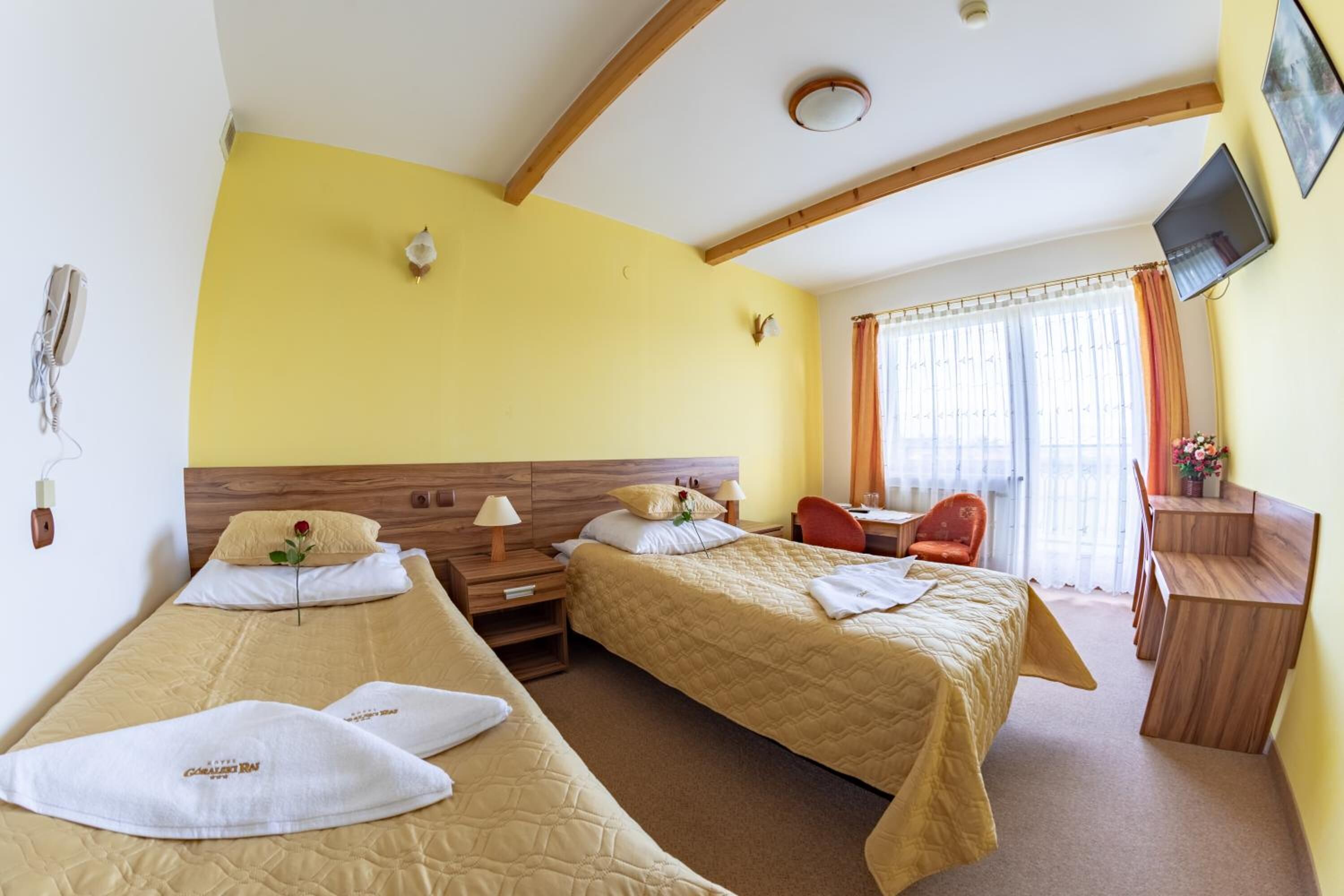 A hotel room with two single beds, a desk, a chair, a television, and a window with curtains.