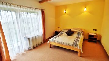 A bedroom with a bed, two bedside tables, a nightstand, a window with curtains, and wall-mounted lights.