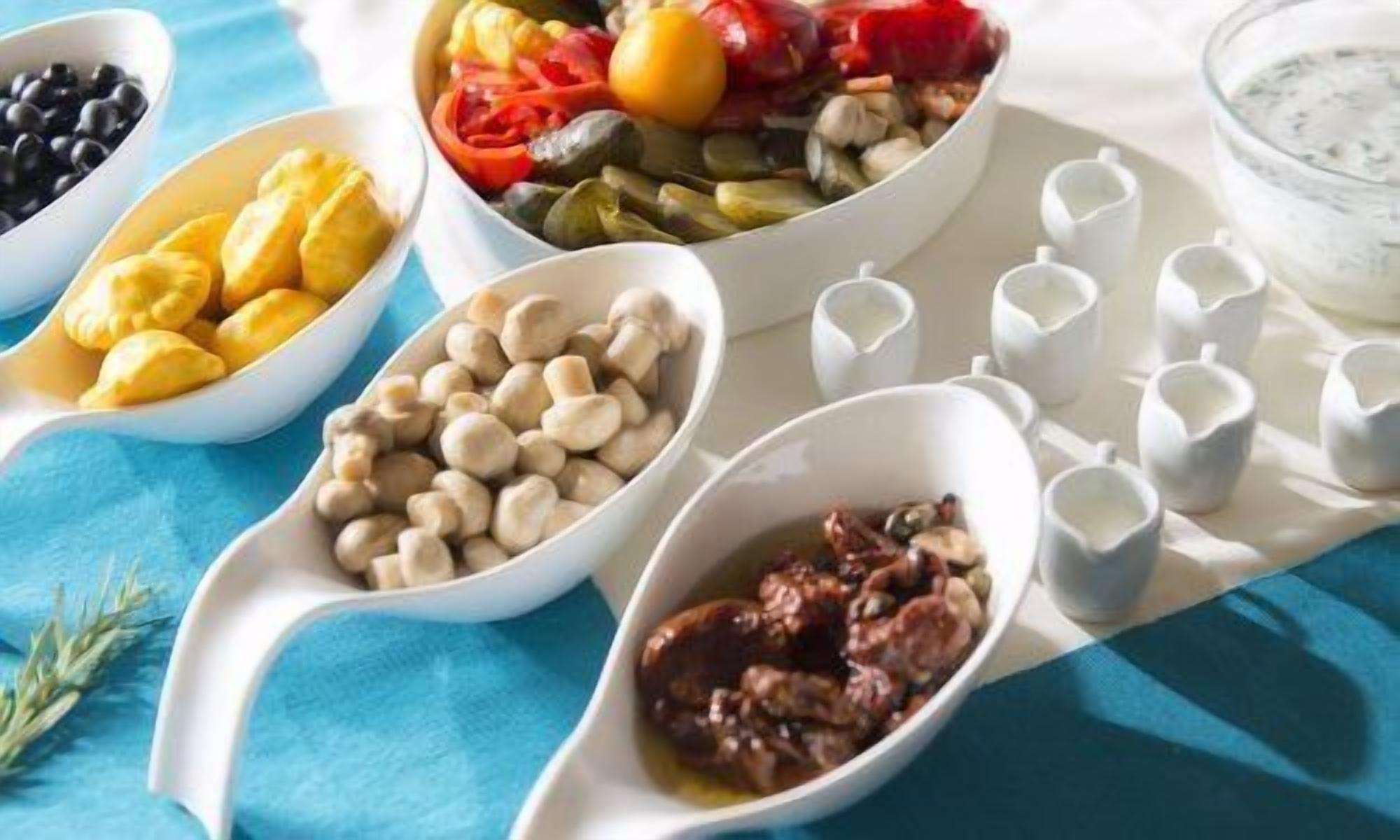 A table with various food items in white bowls and small cups, likely for a meal or buffet setting.