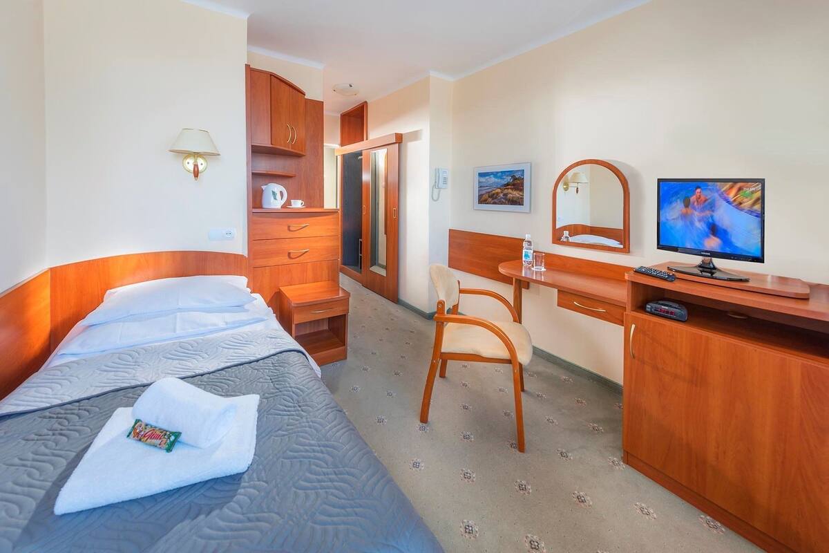 A hotel room with a bed, a desk, a chair, a television, and a wardrobe.