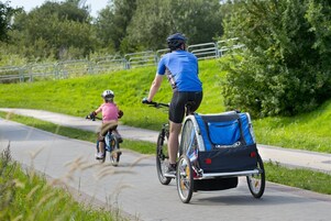 Dos ciclistas en un camino pavimentado, con un remolque azul para bicicletas acoplado a una de las bicicletas.