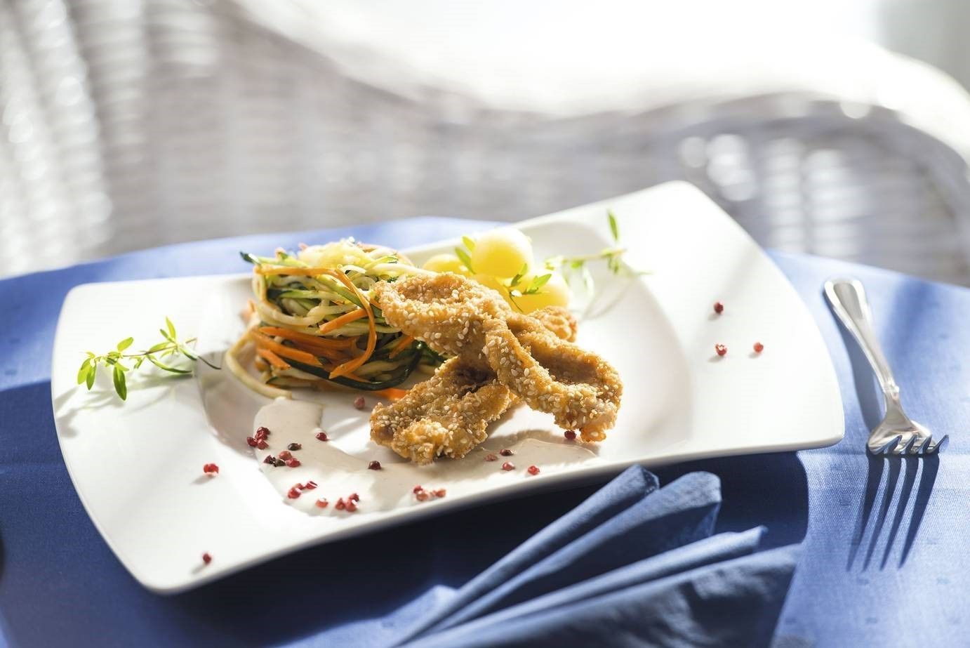 A plate with fried food, a salad, and a lemon wedge on a white plate.