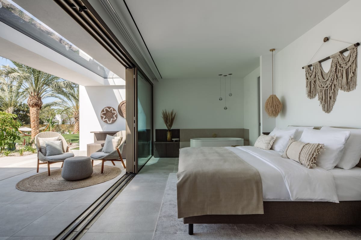 Un dormitorio moderno con una cama grande, una zona de estar con sillas y vistas al exterior.