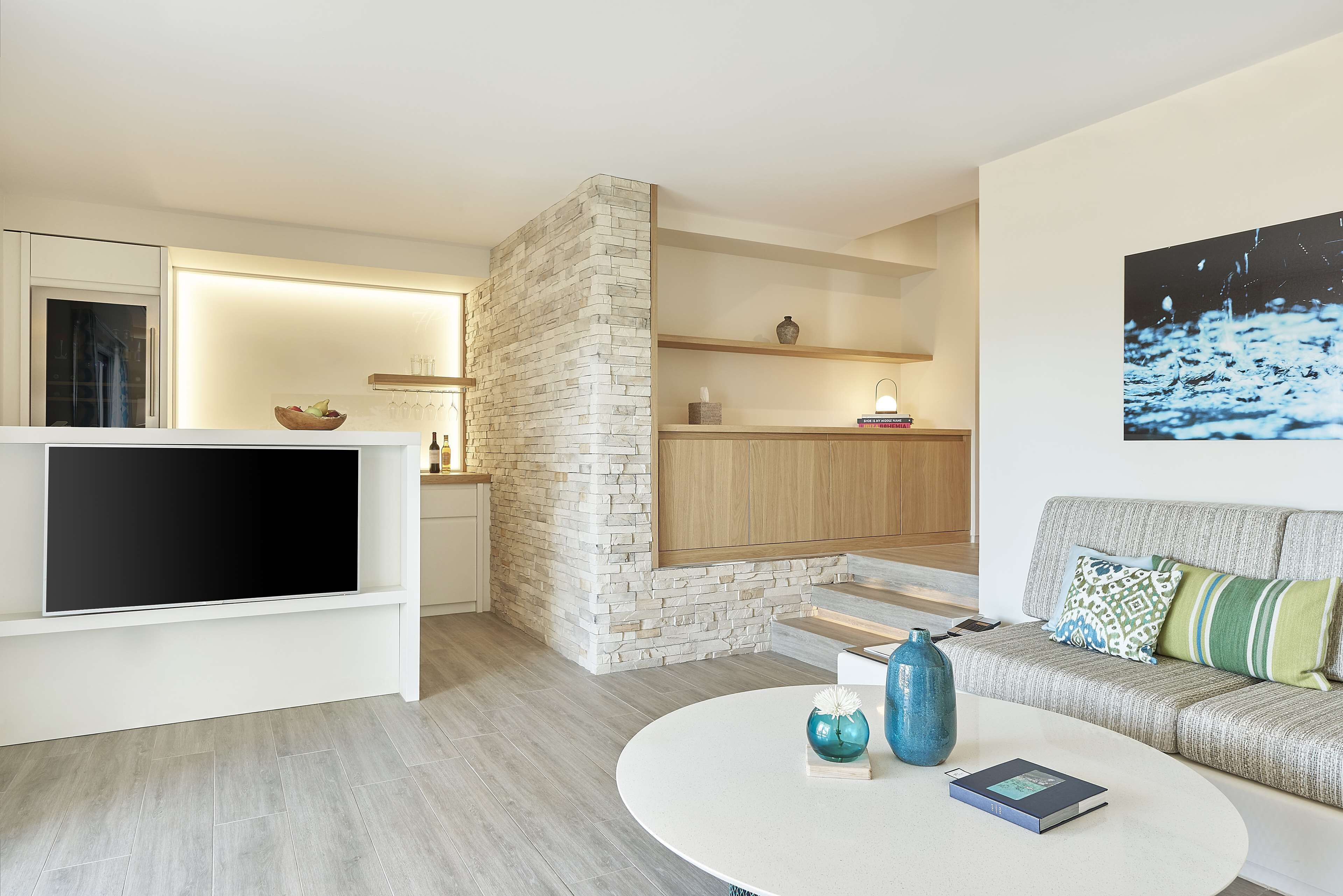 A modern living room with a flat-screen TV, a round coffee table, and a sofa with patterned cushions.