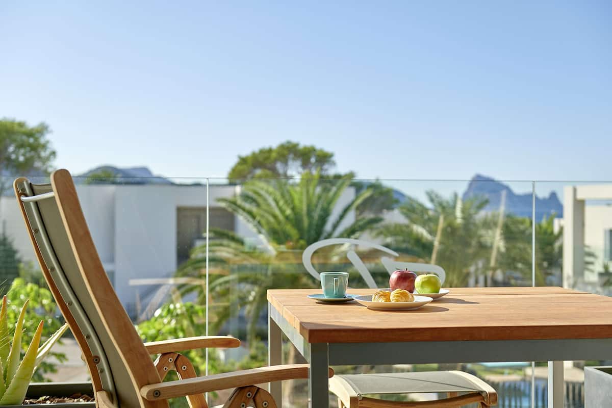 Una mesa de madera con un plato de comida y una taza, una silla, y vistas a palmeras y montañas.