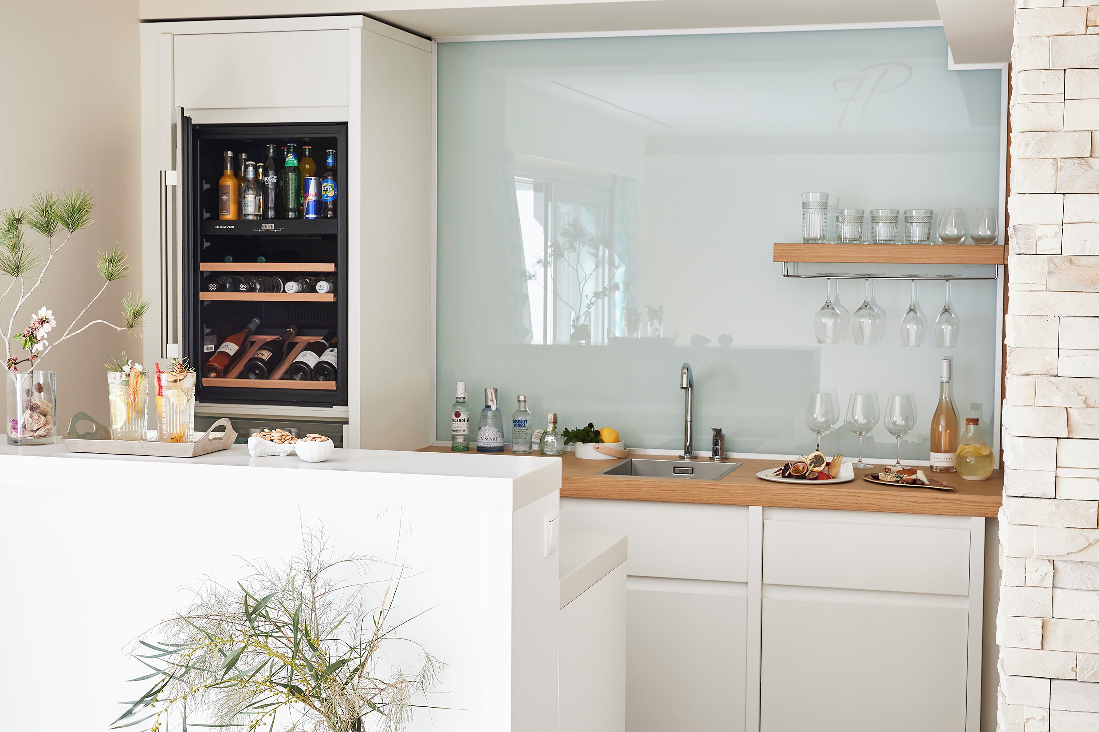 Una cocina moderna con un refrigerador para vinos, copas de vino en un estante y una encimera de madera.