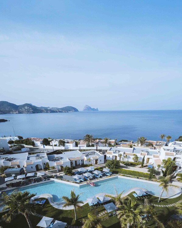 A resort with a pool, white buildings, palm trees, and a view of the sea. - 7Pines Resort Ibiza, part of Destination by Hyatt (Sant Josep de sa Talaia)