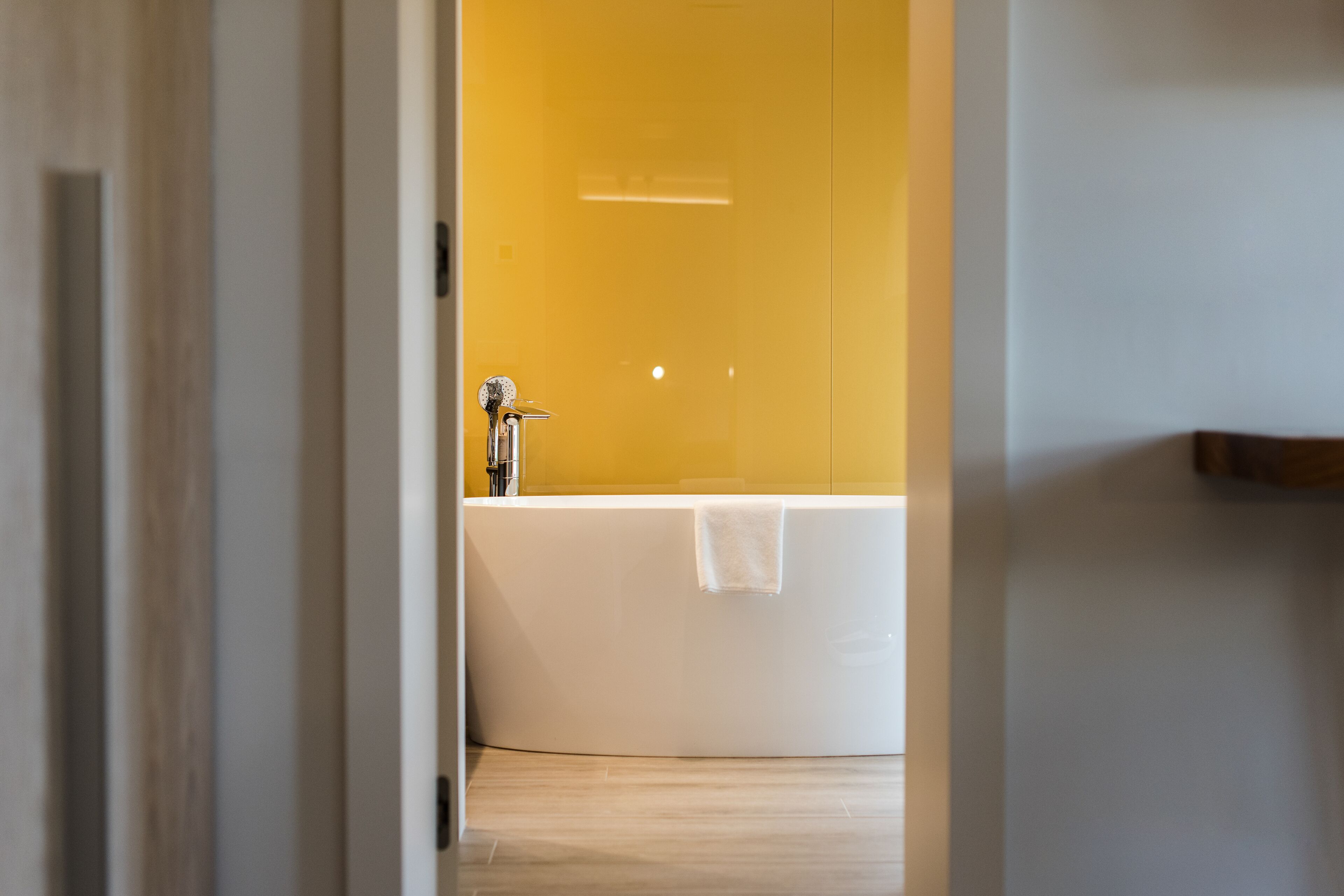 Un baño moderno con una bañera blanca, cabina de ducha de vidrio y pared amarilla.
