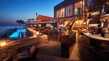 A modern outdoor bar area with a pool, seating, and a view of the sea.