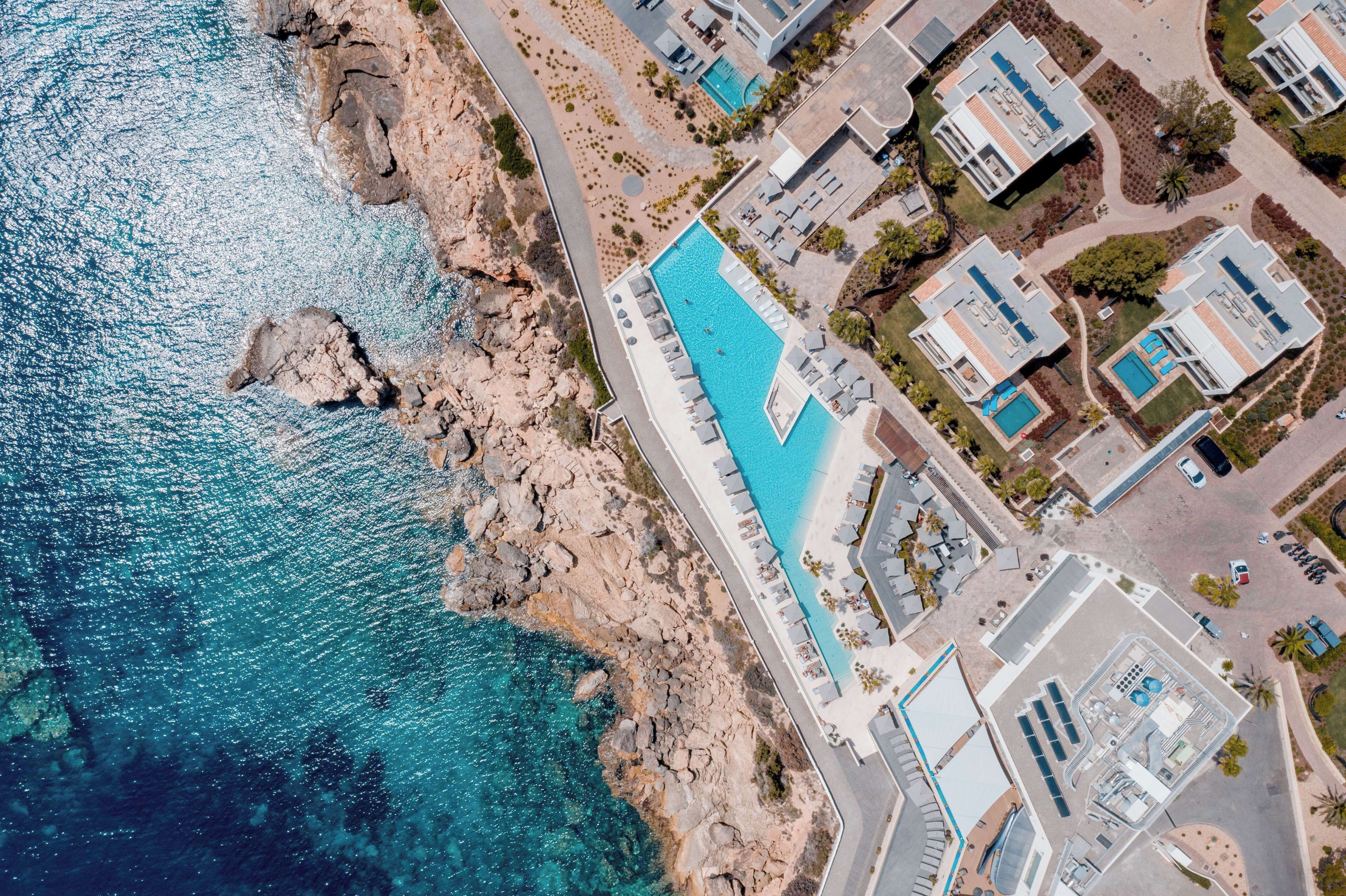 Vista aérea de una propiedad costera con piscina, edificios modernos y terreno rocoso.